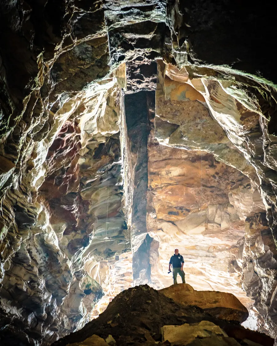 A worker dwarfed by a vast underground stope, mineral-streaked rock rising above